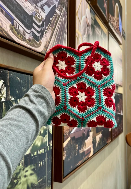 Red and turquoise crochet tote held in a gallery